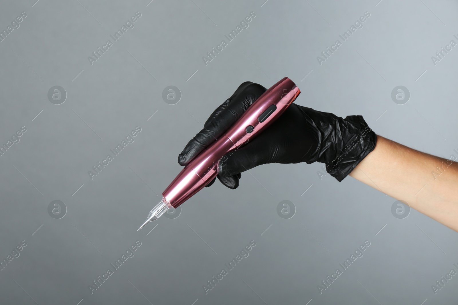 Photo of Professional cosmetologist holding permanent makeup machine on grey background, closeup