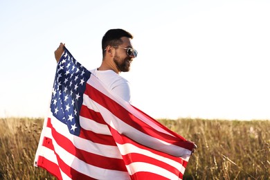 Photo of Happy man with flag of USA outdoors, back view. Space for text