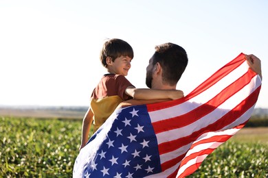 Photo of Father and son with flag of USA outdoors, back view