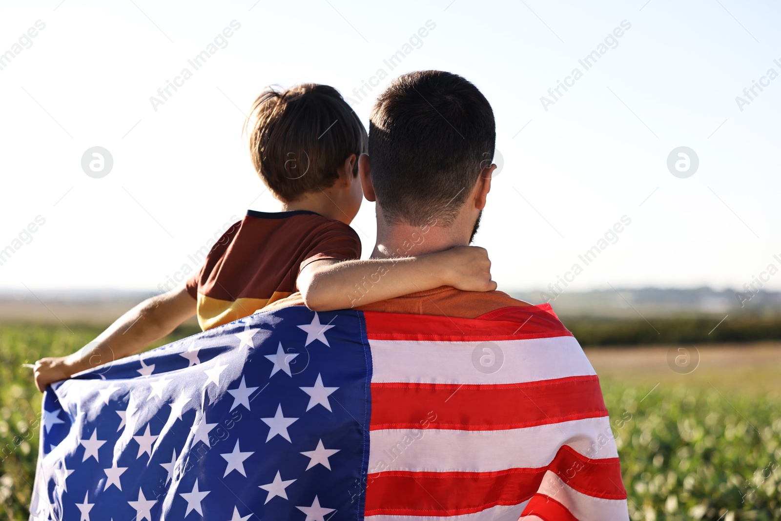 Photo of Father and son with flag of USA outdoors, back view