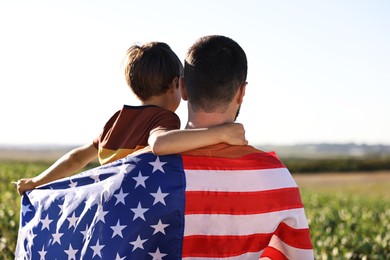 Photo of Father and son with flag of USA outdoors, back view