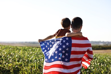 Photo of Father and son with flag of USA outdoors. back view. Space for text