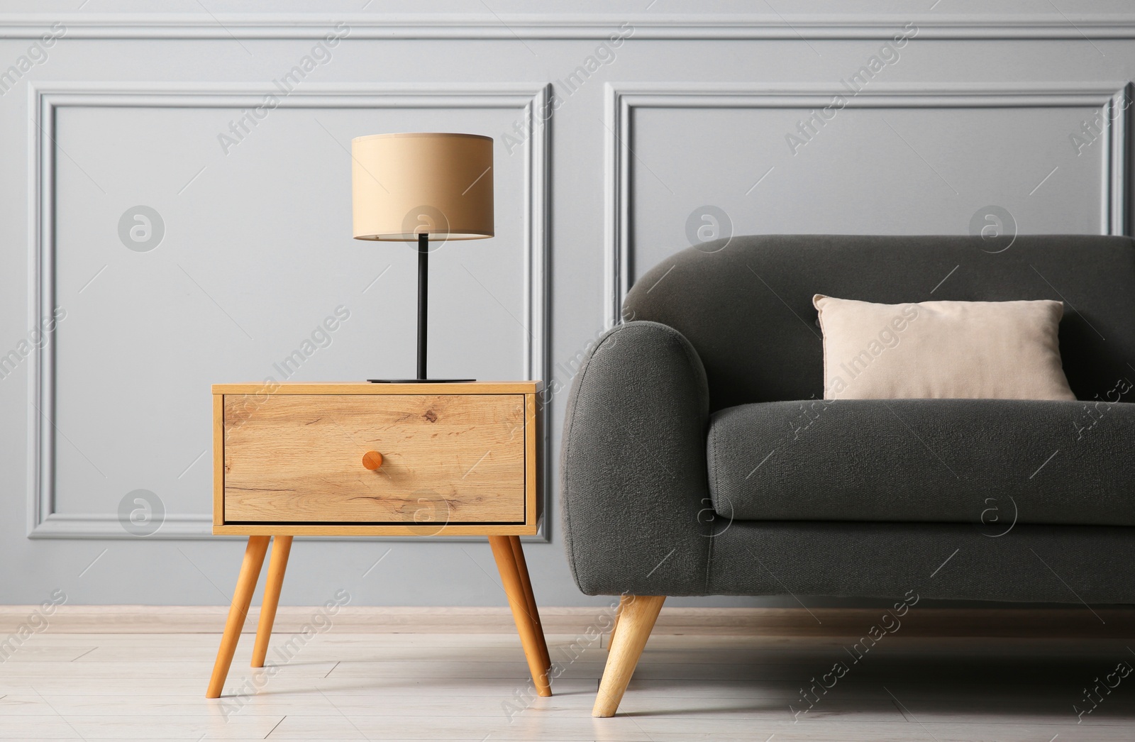 Photo of Stylish sofa with cushion and lamp on side table near grey wall