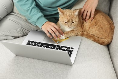 Online pet shop. Woman with laptop, credit card and cute cat making order on sofa at home, closeup