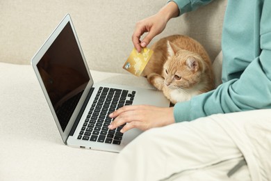 Online pet shop. Woman with laptop, credit card and cute cat making order on sofa at home, closeup