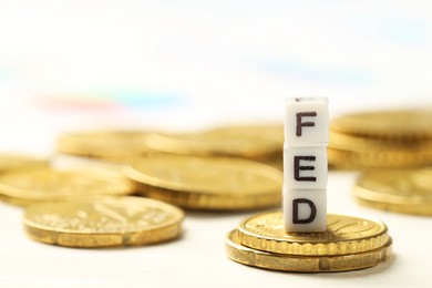 Photo of Cubes with letters Fed (Federal Reserve System) and coins on white table, closeup. Space for text