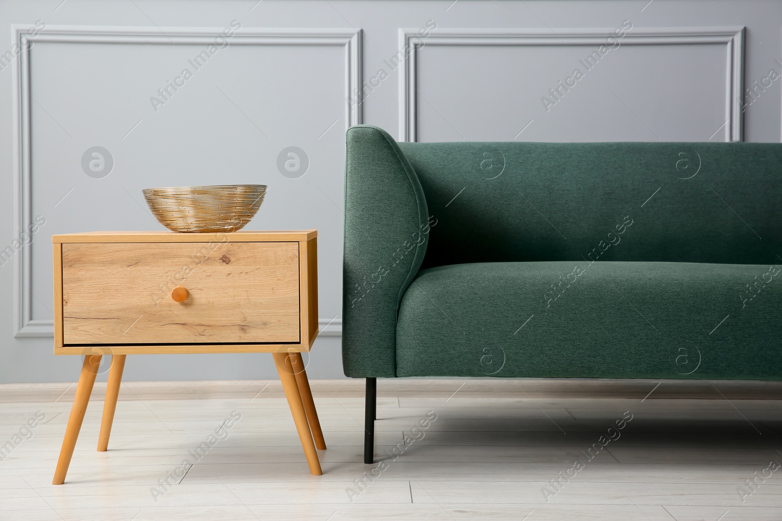 Photo of Stylish sofa and bowl on side table near grey wall