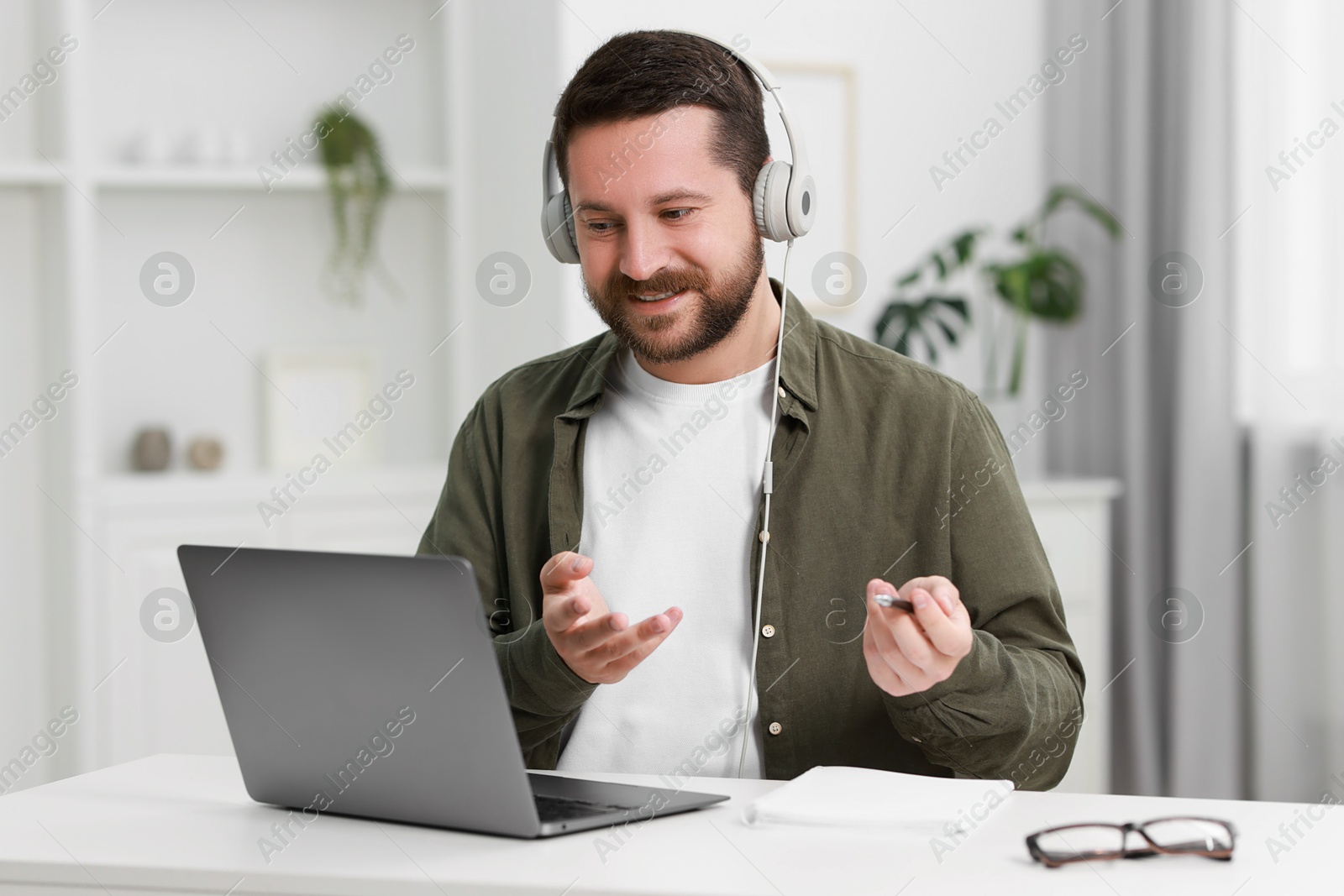 Photo of Interpreter in headphones having video chat via laptop at white table indoors