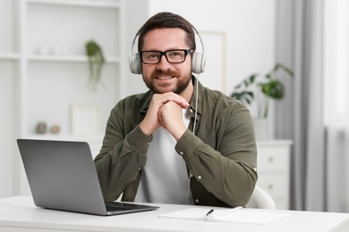 Photo of Interpreter in headphones having video chat via laptop at white table indoors