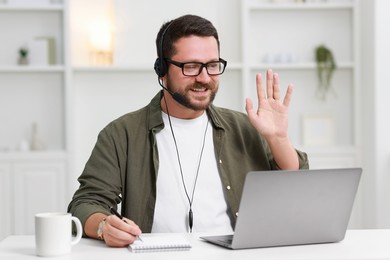 Interpreter in headset having video chat via laptop at white table indoors