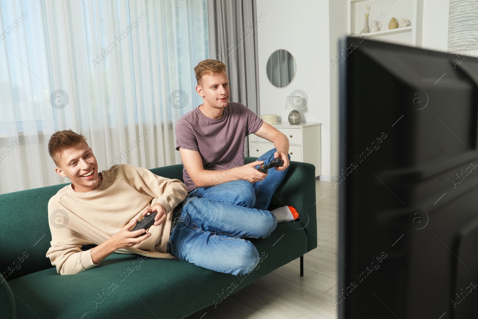 Photo of Happy brothers playing video game on sofa at home