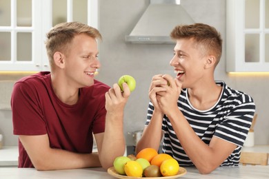 Happy brothers eating apples at table in kitchen