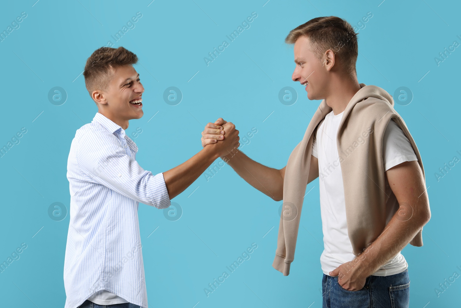 Photo of Happy brothers clasping hands on light blue background