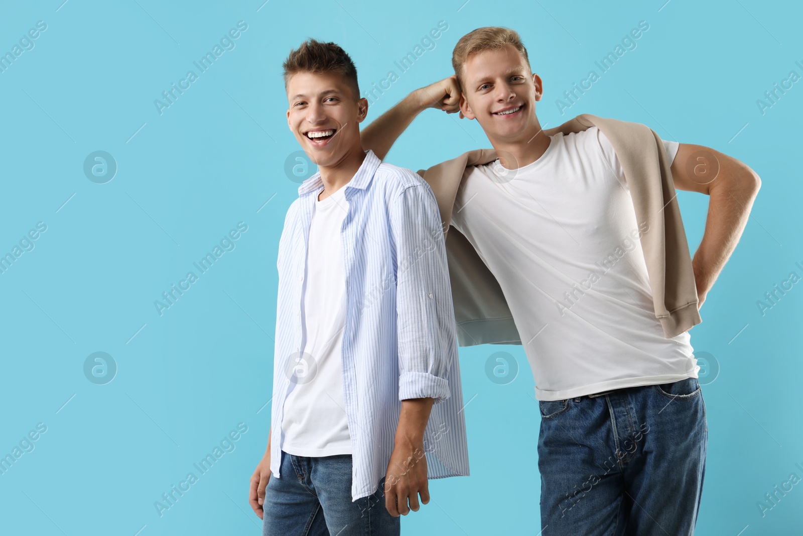 Photo of Happy brothers posing on light blue background. Space for text