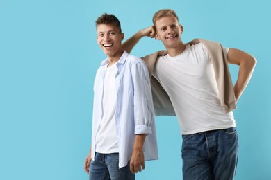 Photo of Happy brothers posing on light blue background. Space for text