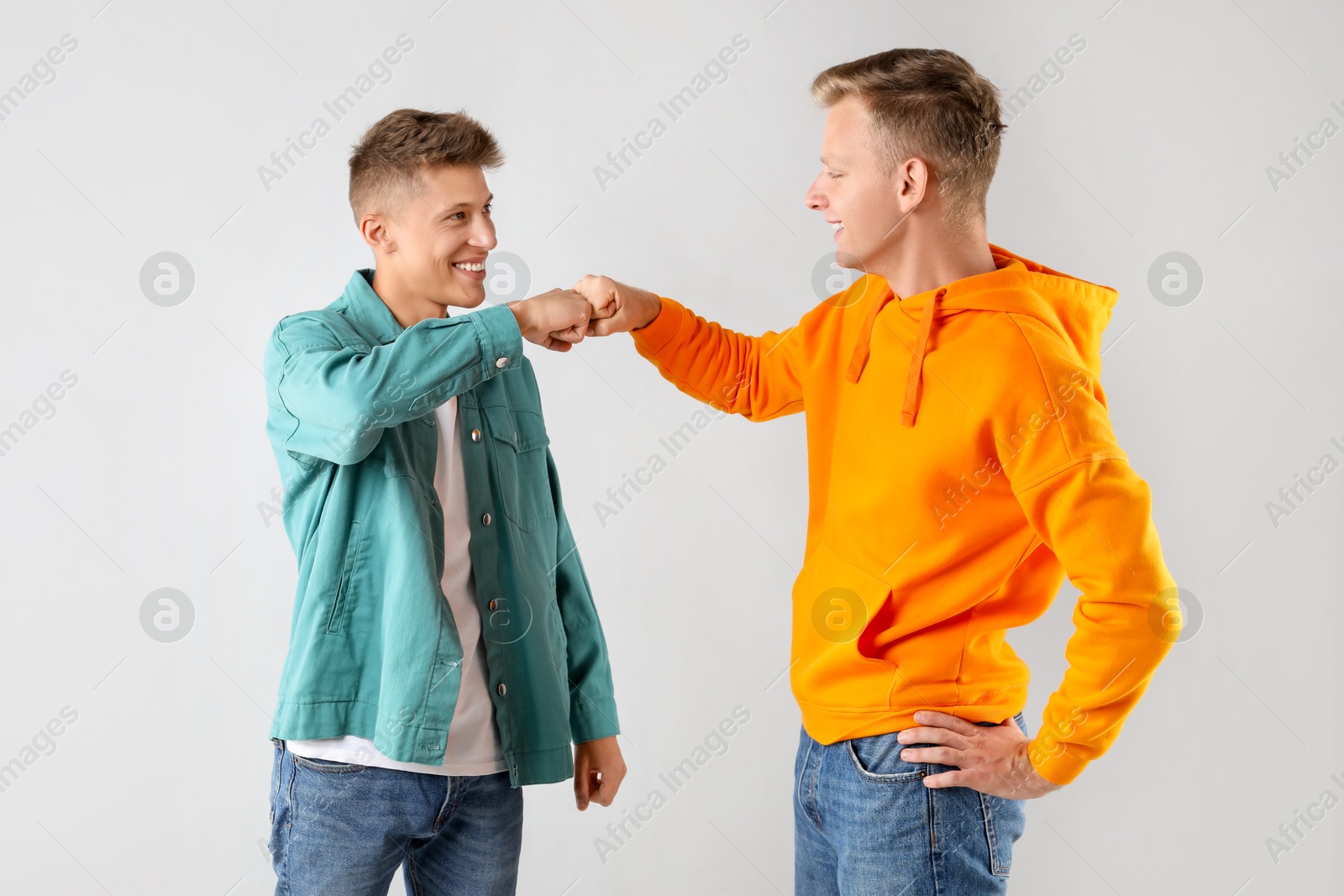 Photo of Two happy brothers making fist bump on light background. Space for text