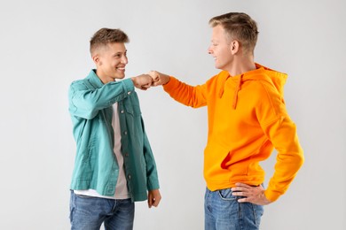 Photo of Two happy brothers making fist bump on light background. Space for text