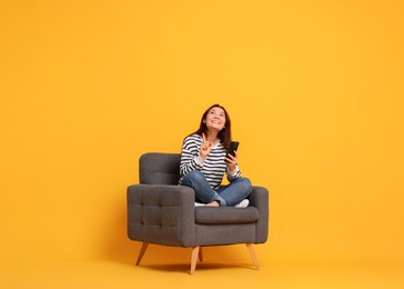 Photo of Smiling woman with smartphone sitting in armchair on yellow background