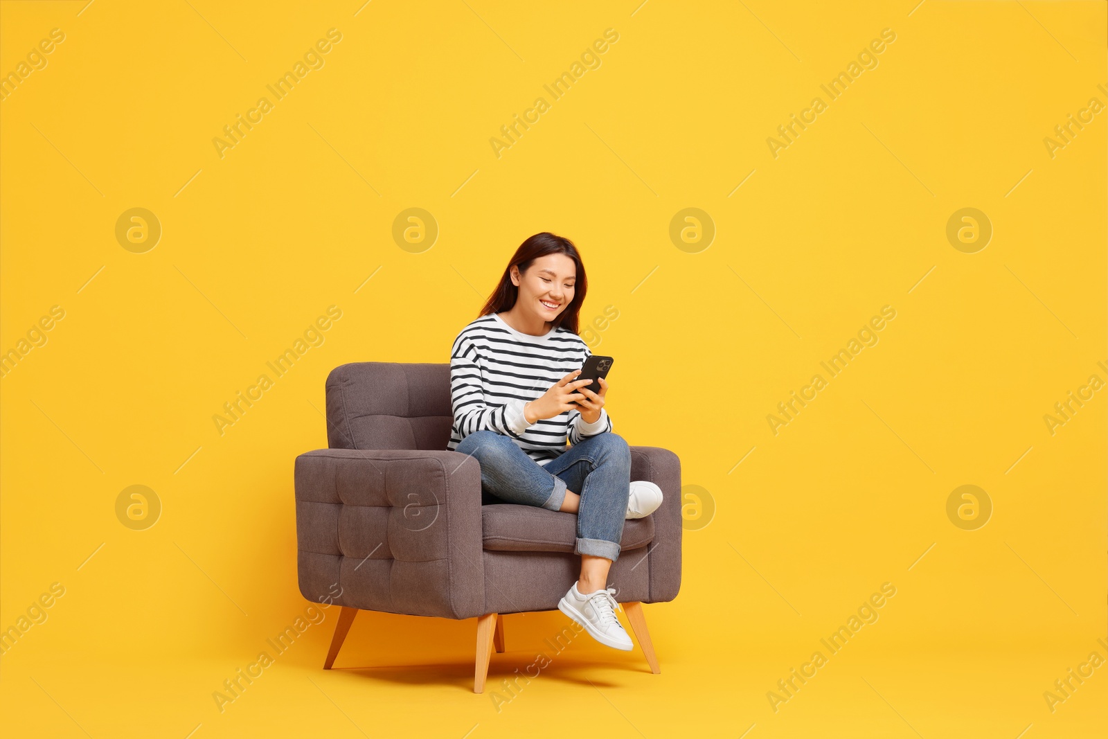 Photo of Smiling woman with smartphone sitting in armchair on yellow background