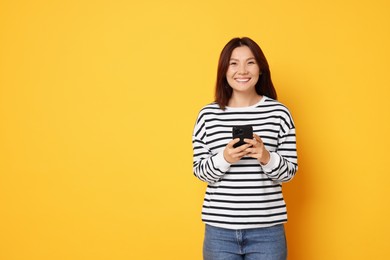 Photo of Smiling young woman with smartphone on yellow background. Space for text