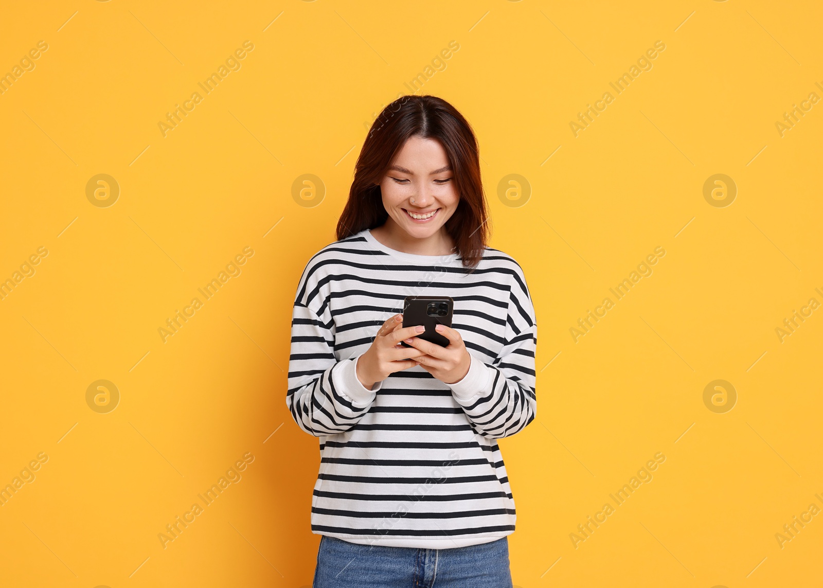 Photo of Smiling young woman using smartphone on yellow background