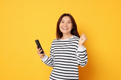 Smiling young woman with smartphone on yellow background