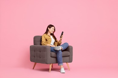 Photo of Smiling woman with smartphone sitting in armchair on pink background