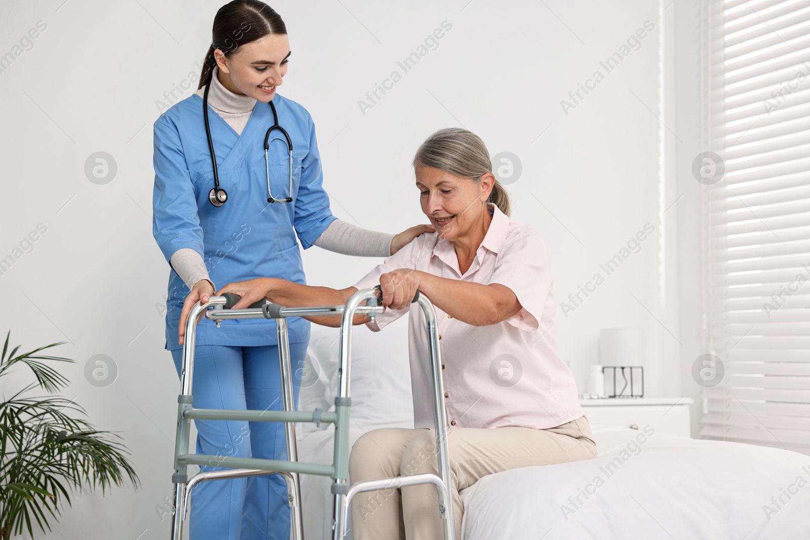 Photo of Nurse helping senior woman with walking frame in clinic