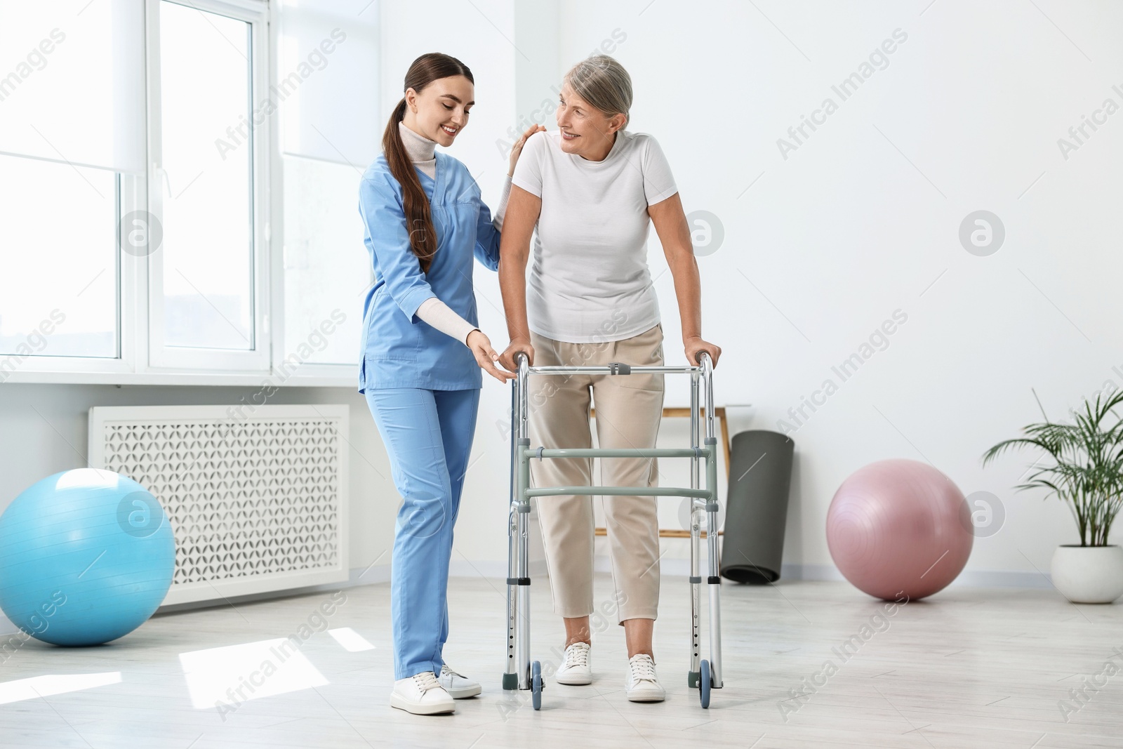 Photo of Nurse helping senior woman with walking frame in clinic