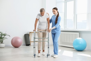 Photo of Nurse helping senior woman with walking frame in clinic