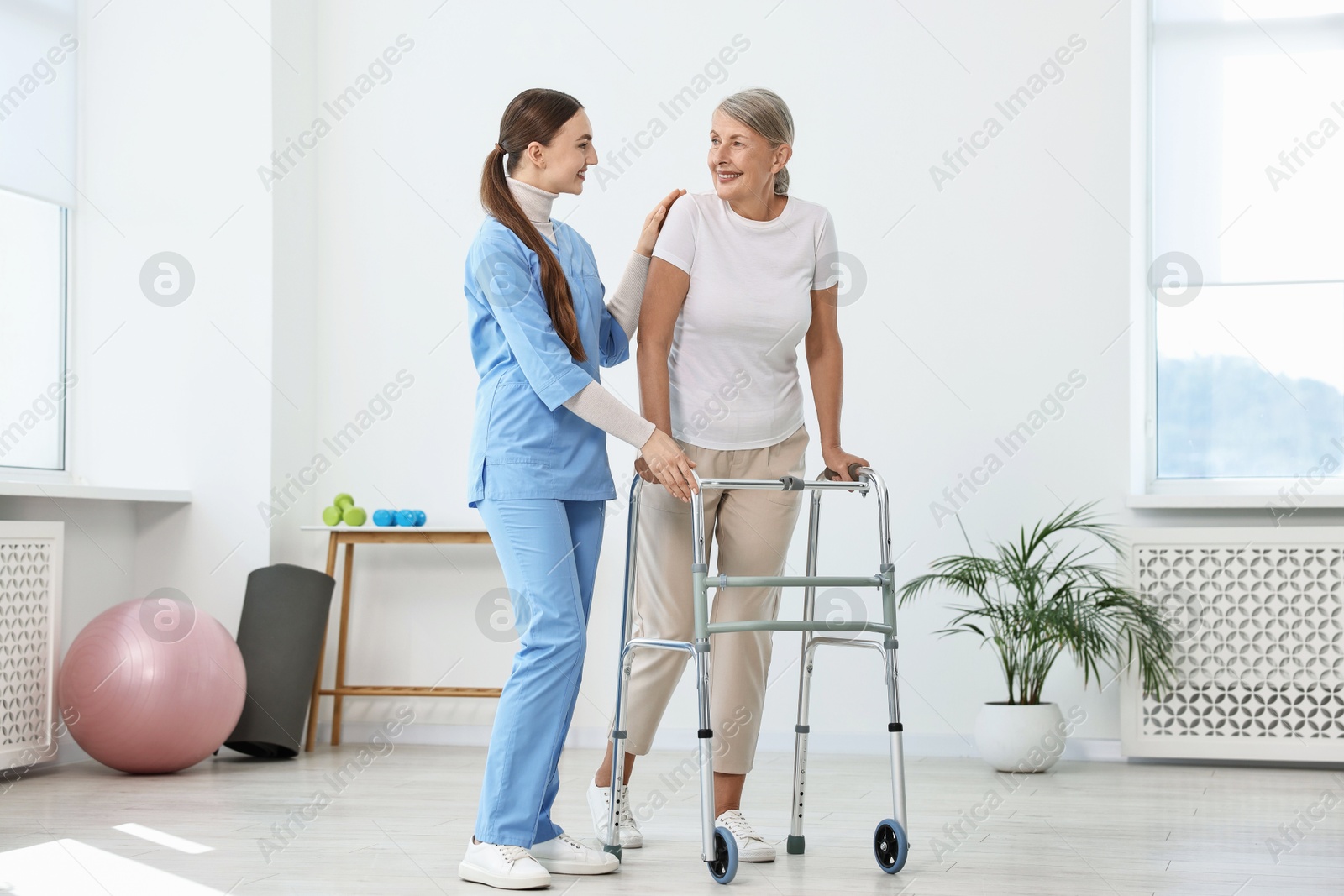 Photo of Nurse helping senior woman with walking frame in clinic