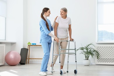 Nurse helping senior woman with walking frame in clinic