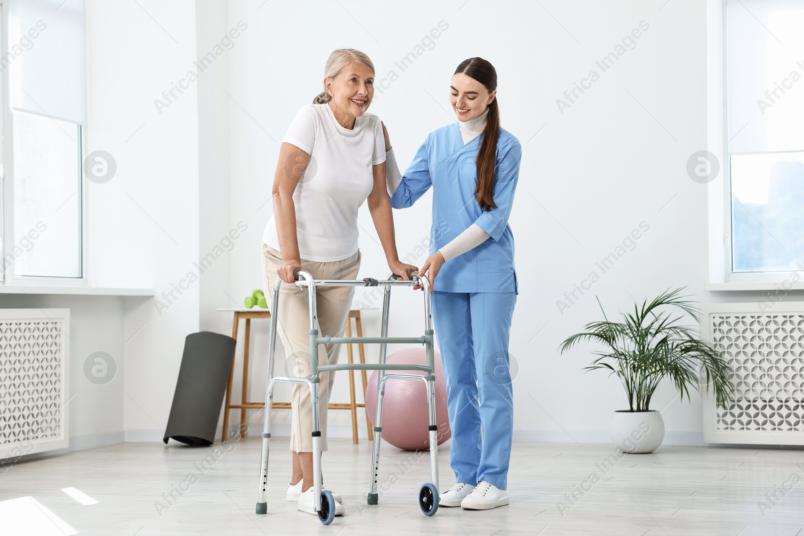 Photo of Nurse helping senior woman with walking frame in clinic