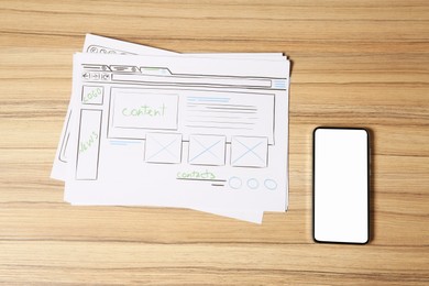 Photo of Website development. Sketches of wireframes and smartphone on wooden table, flat lay