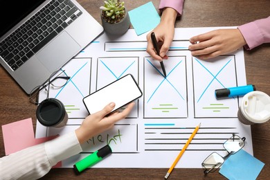 Photo of Developing UI design. Designers creating website wireframe on paper at wooden table, top view