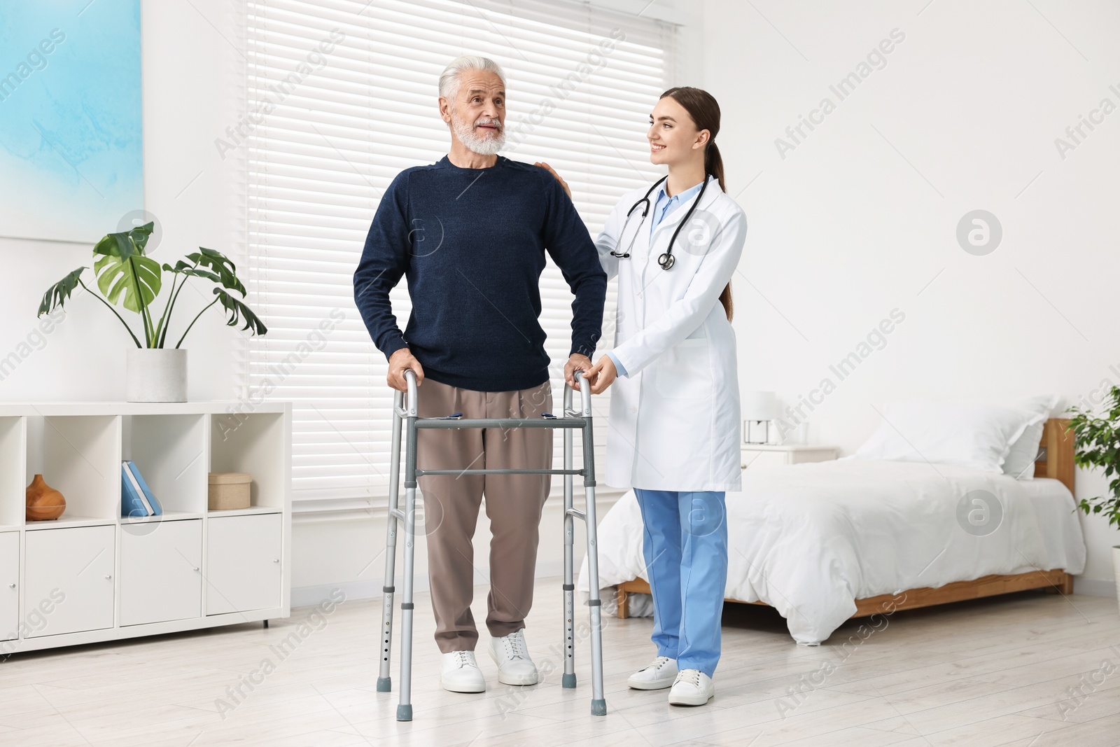 Photo of Doctor helping senior man with walking frame in clinic