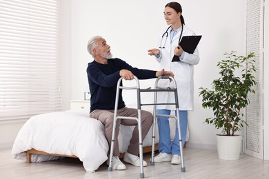 Photo of Doctor consulting senior patient with walking frame in hospital ward