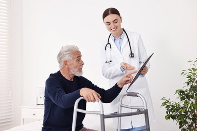 Photo of Doctor consulting senior patient with walking frame in hospital ward