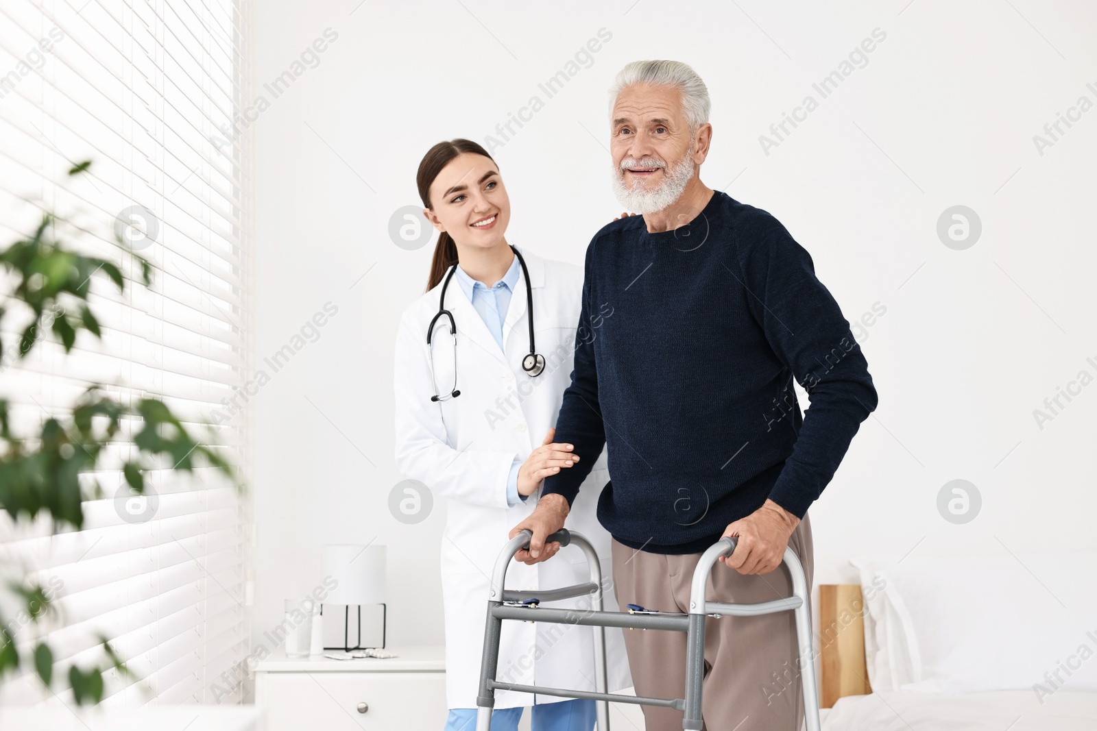 Photo of Doctor helping senior man with walking frame in clinic