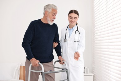 Doctor helping senior man with walking frame in clinic