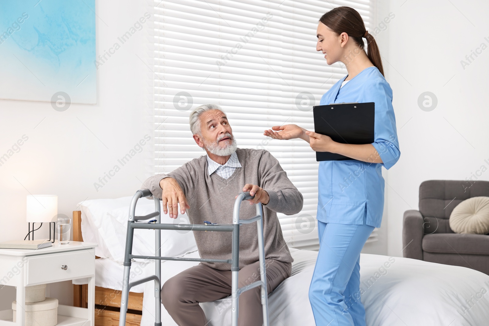 Photo of Doctor consulting senior patient with walking frame in hospital ward