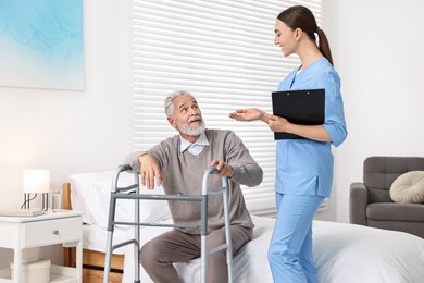 Photo of Doctor consulting senior patient with walking frame in hospital ward