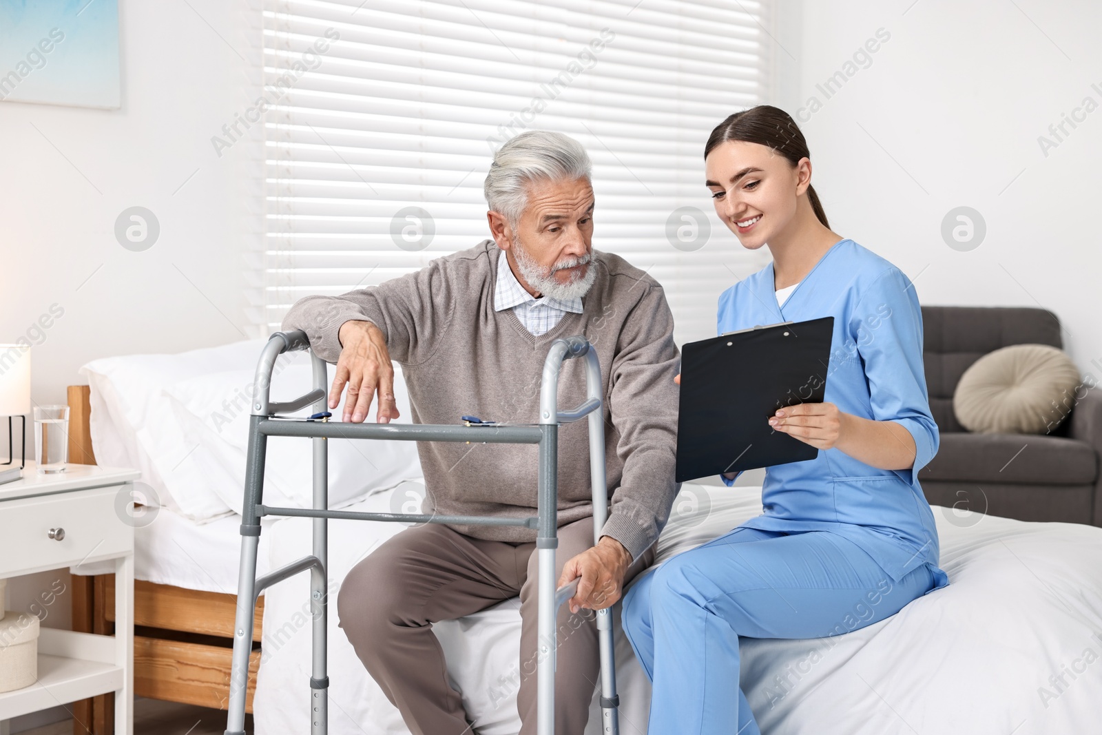 Photo of Doctor consulting senior patient with walking frame in hospital ward