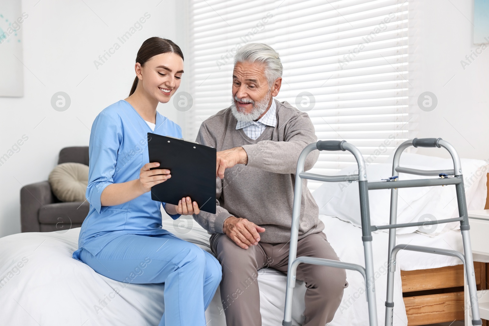 Photo of Doctor consulting senior patient with walking frame in hospital ward