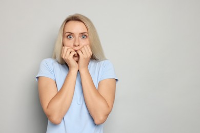 Portrait of scared woman on gray background, space for text