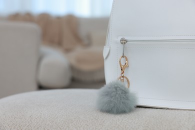 Photo of Stylish backpack with faux fur keychain on soft surface indoors, closeup. Space for text