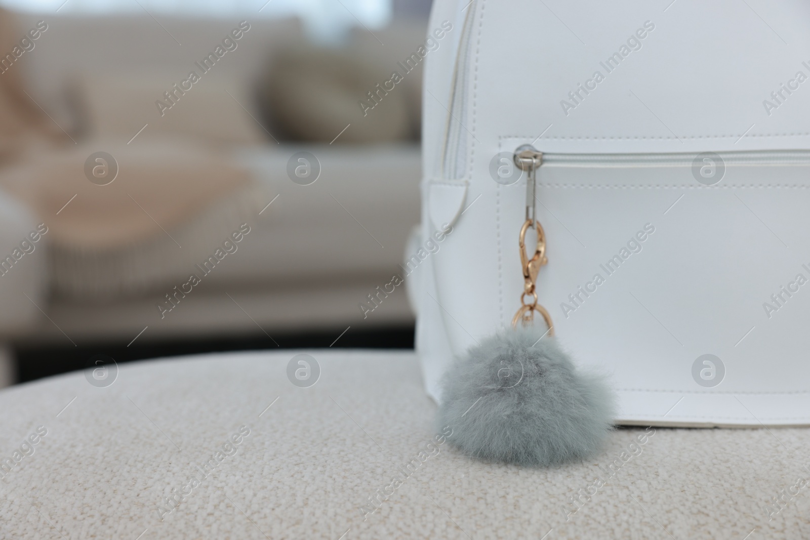 Photo of Stylish backpack with faux fur keychain on soft surface indoors, closeup. Space for text