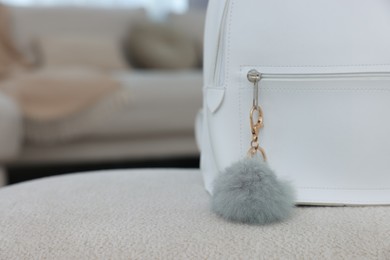 Photo of Stylish backpack with faux fur keychain on soft surface indoors, closeup. Space for text