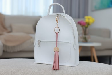 Photo of Stylish backpack with pink leather keychain on soft surface indoors