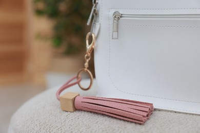 Photo of Stylish backpack with pink leather keychain on soft surface indoors, closeup